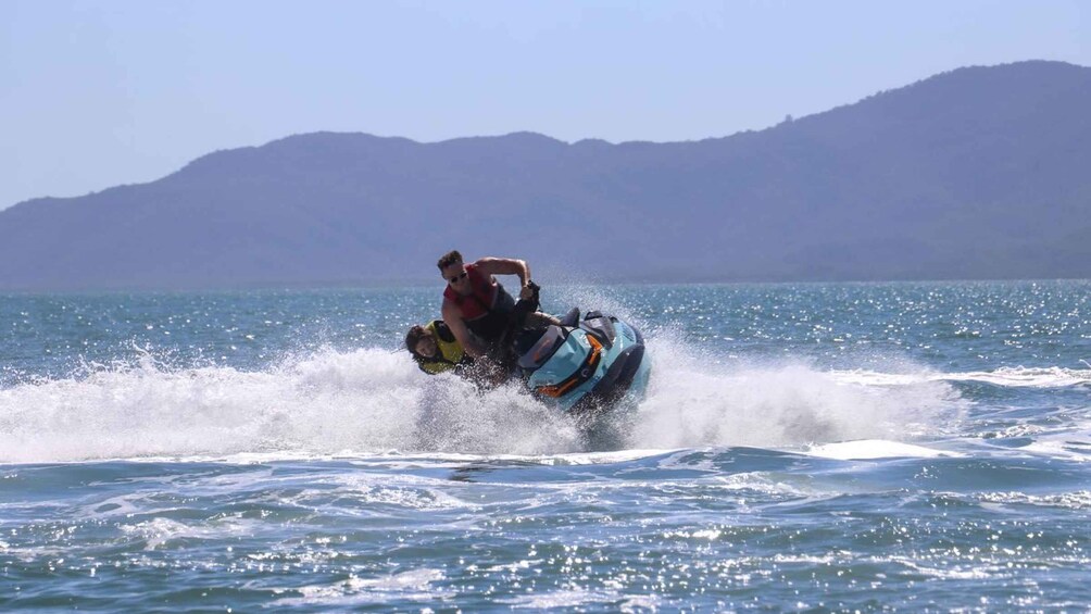 En person kører på en jetski på vandet med bølger, iført redningsvest, og et bjergrigt landskab i baggrunden. 1