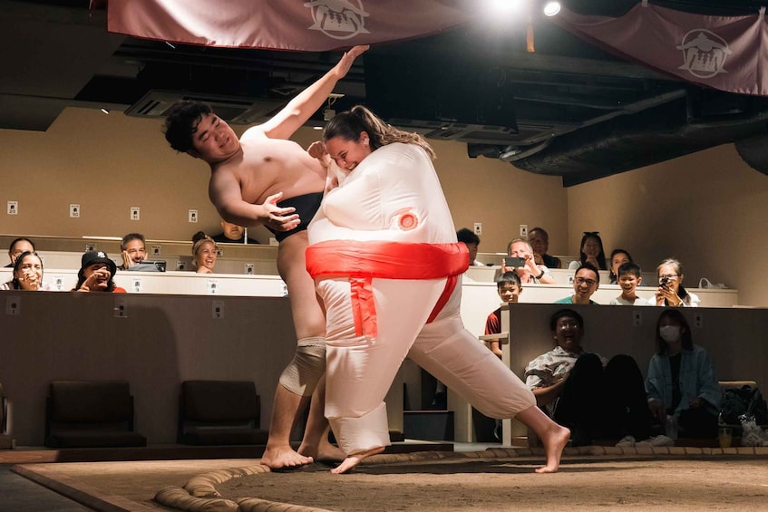 A sumo wrestling match with a referee and a crowd watching. 3