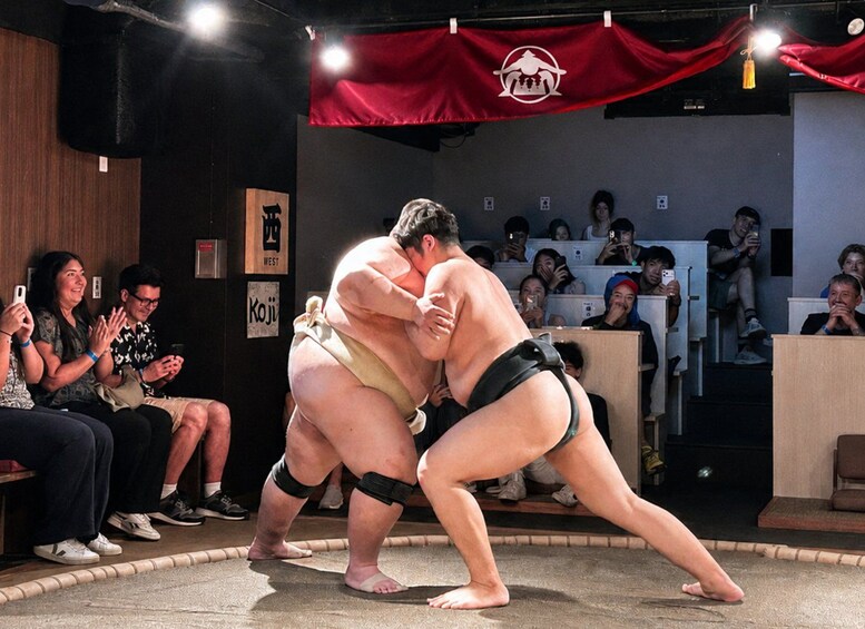 Two sumo wrestlers in a ring, surrounded by spectators. 1
