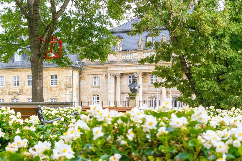 A historic building with classical architecture, surrounded by lush greenery and white flowers. 1