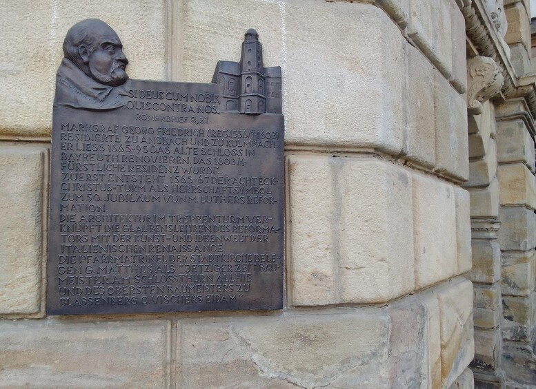 A stone plaque with a bust and text, mounted on a building wall. 2