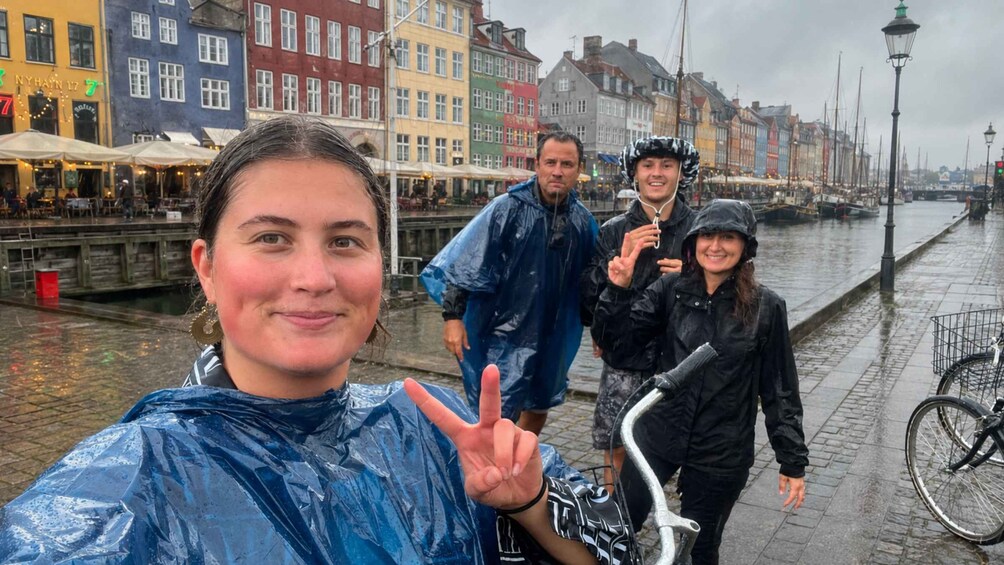 Ryhmä ihmisiä ottaa selfien sateisena päivänä kanavan varrella, ja taustalla näkyy värikkäitä rakennuksia. 1
