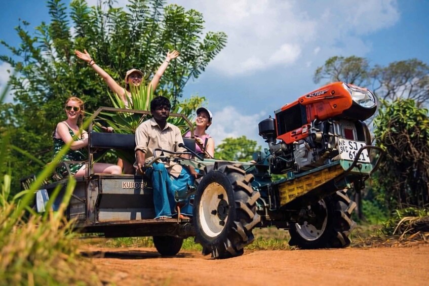 Eine Gruppe von Personen fährt mit einem Kubota-Traktor samt Anhänger auf einem Feldweg, umgeben von viel Grün. 5