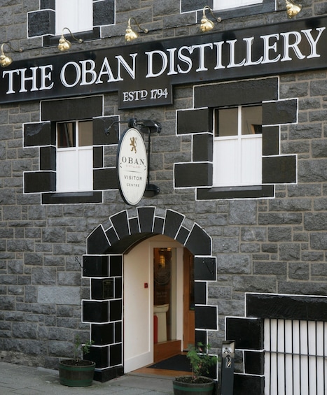 The Oban Distillery with a stone facade, a visitor center sign, and a small entrance. 1