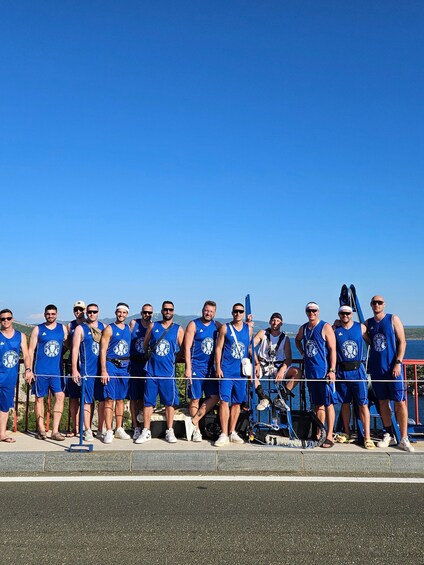 A group of people in blue athletic wear standing on a dock by the water. 2