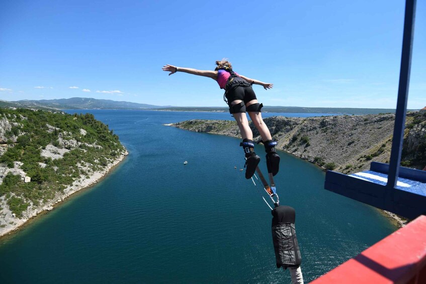 A person bungee jumping off a bridge with a scenic view of a body of water and hills in the background. 1