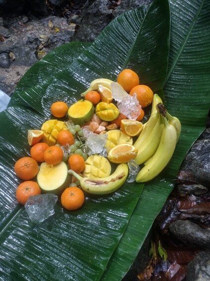 A variety of fruits including mangoes, oranges, and bananas arranged on a green leaf. 5