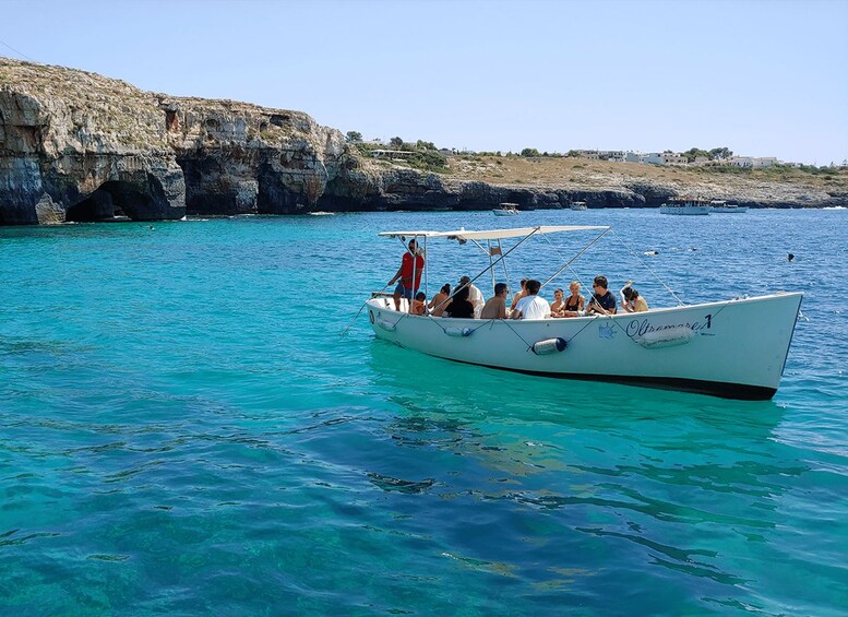 A boat with passengers on a turquoise sea, rocky cliffs in the background. 1