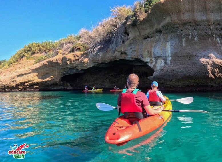 Personas haciendo kayak en un mar azul cristalino con un acantilado rocoso al fondo. 2