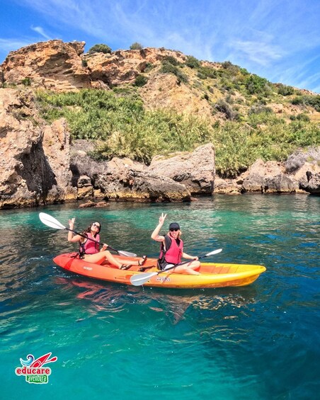 Dos personas hacen kayak en un mar turquesa y transparente, con acantilados rocosos al fondo. 3