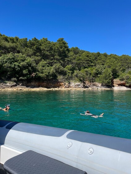 A boat with people swimming in clear turquoise water, surrounded by a forested coastline. 4