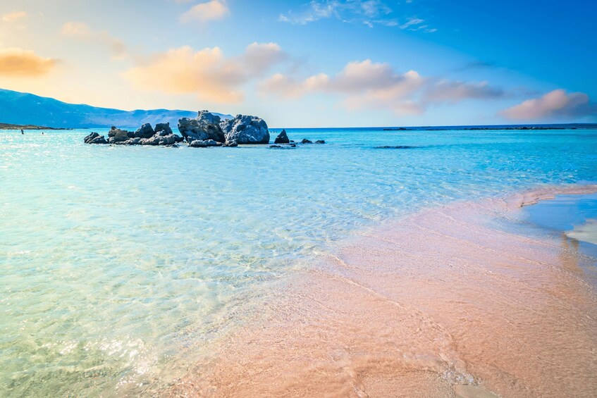 Ein Strand mit klarem türkisblauem Wasser, einem Sandstrand und einem Felsen im Hintergrund. 2