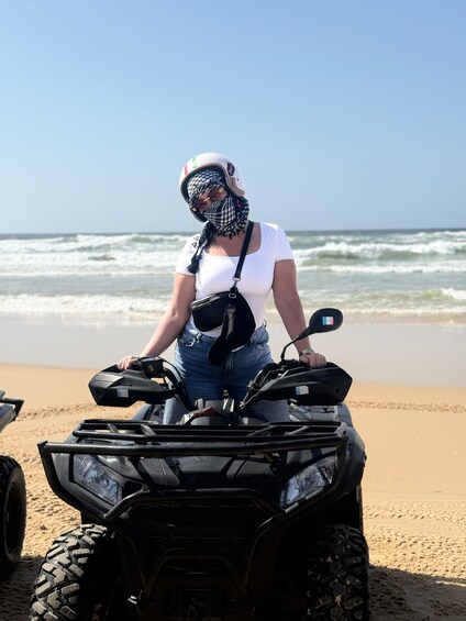 A person standing next to an ATV on a sandy beach with waves in the background. 4