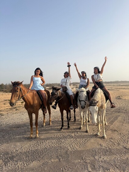 Four people riding horses on a dirt path in a desert landscape. 2