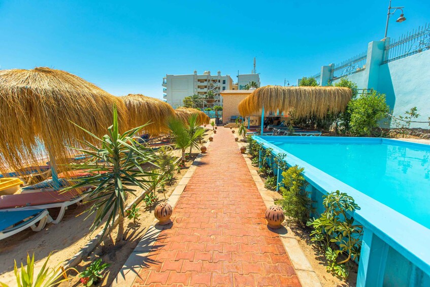 A poolside area with a brick pathway, lounge chairs, and thatched umbrellas. 2