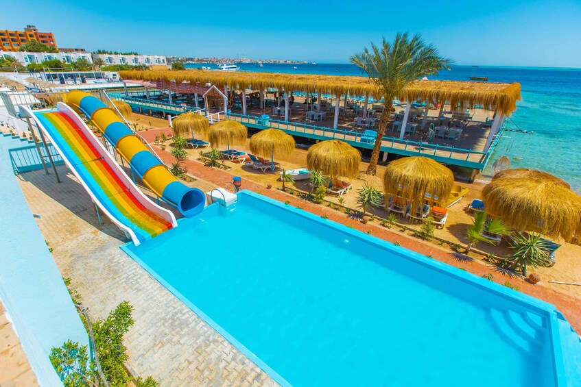 A swimming pool with a rainbow slide, lounge chairs, and thatched umbrellas. 1