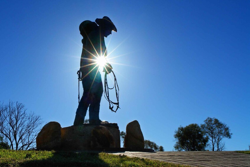 Eine Statue einer Person, die ein Pferd hält, steht auf einem Felsen, im Hintergrund scheint eine helle Sonne. 1