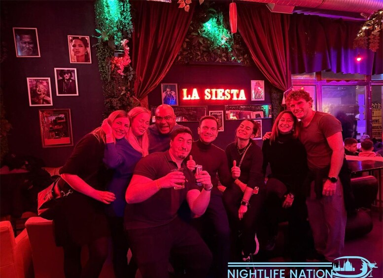 A group of people posing in a dimly lit room with a sign that reads 'LA SISTA'. 2