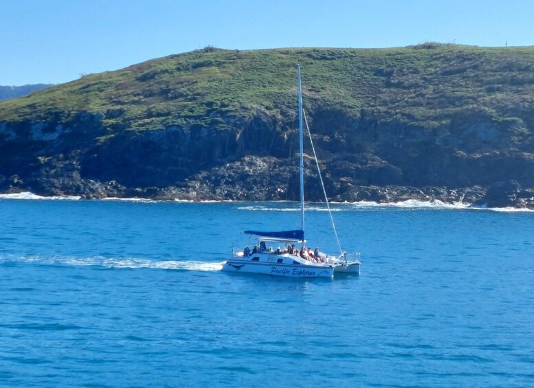 A sailboat named 'Pacific Explorer' on a calm sea with a rocky coastline and a hill in the background. 2