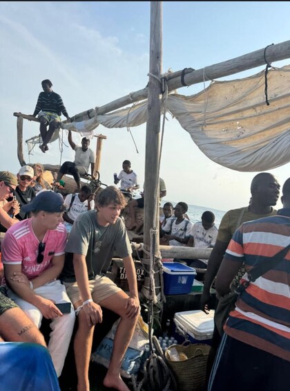 A group of people on a boat with a makeshift shelter and various items like a cooler and bags. 5