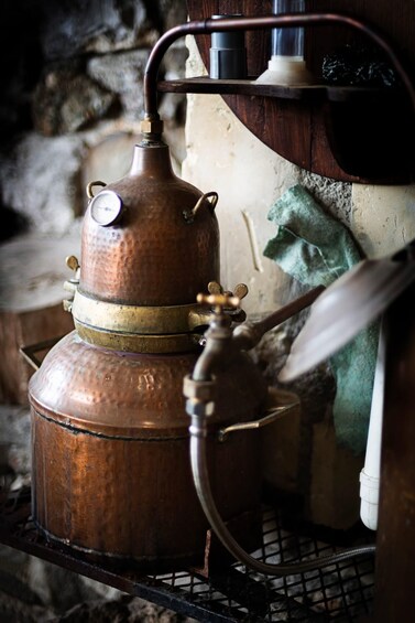 An antique copper distillation apparatus with a thermometer, a spigot, and a glass container. 2