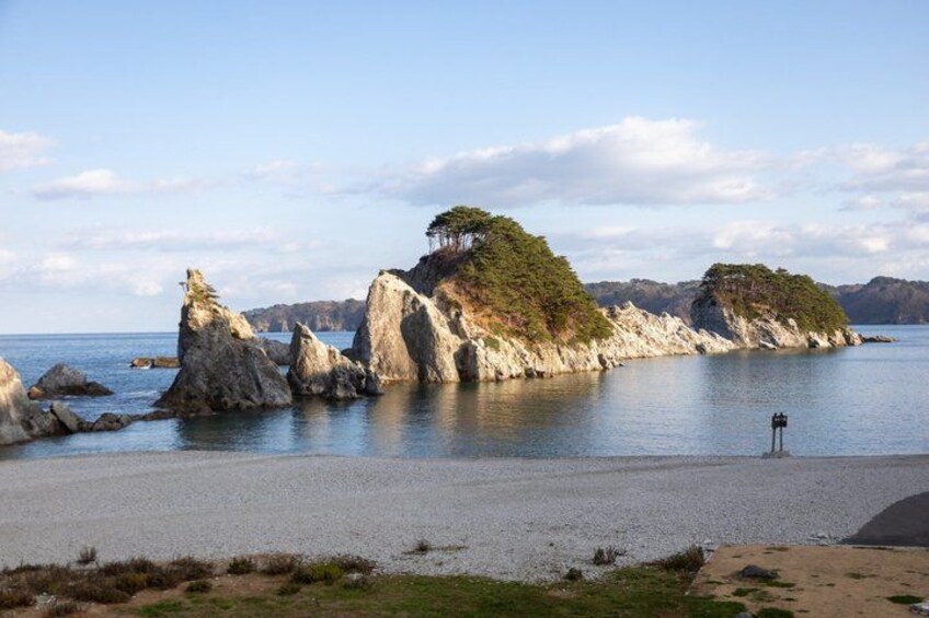 A coastal landscape with rocky outcrops, calm water, and a clear sky. 3