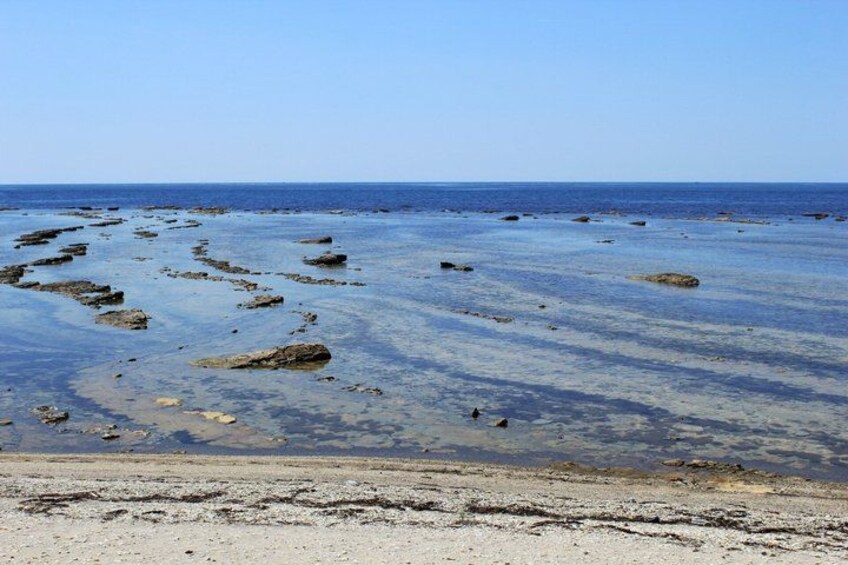 A beach with scattered rocks and clear blue water. 4