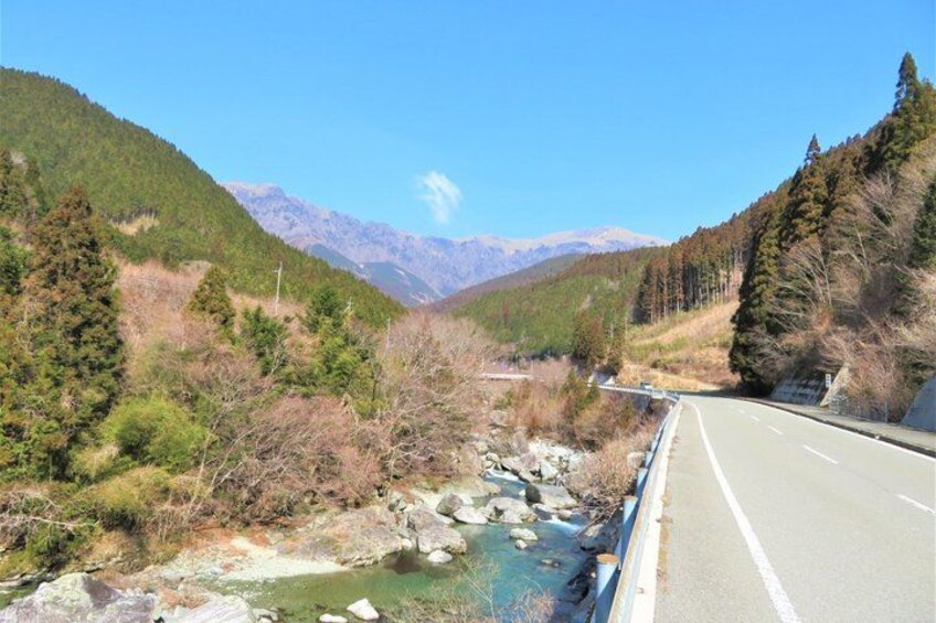A road with a river on the left, surrounded by mountains and trees. 1