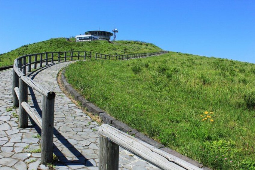 A winding stone pathway with wooden railings, leading to a building on a grassy hill. 3