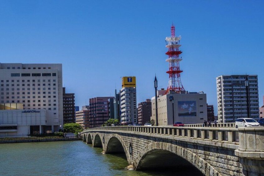 A stone bridge over water, a red and white tower, and modern buildings. 5