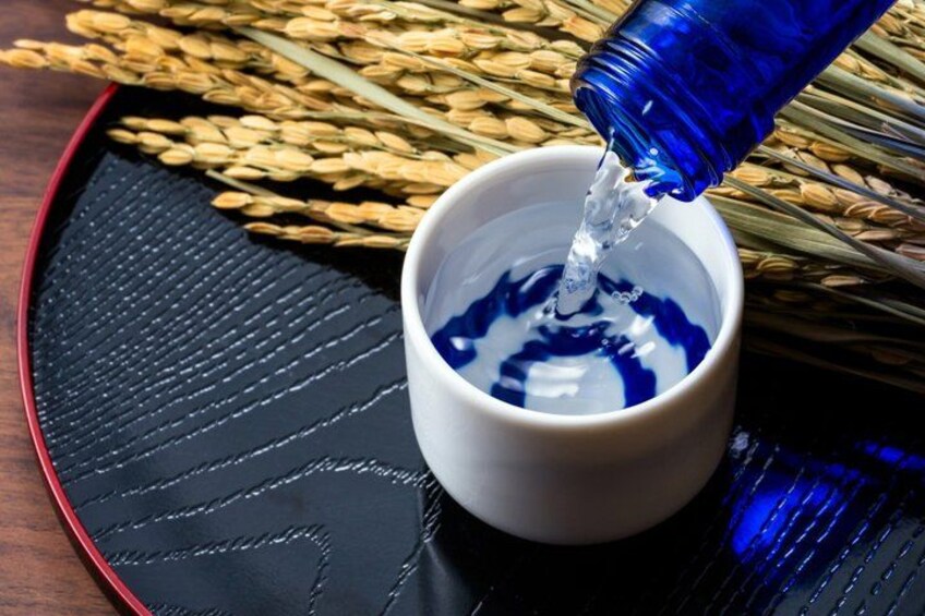 A white cup on a black tray with blue liquid being poured into it. 2