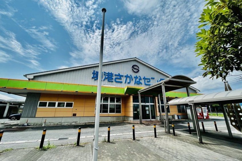 A building with a sign in a foreign language, a covered walkway, and bollards along the sidewalk. 2