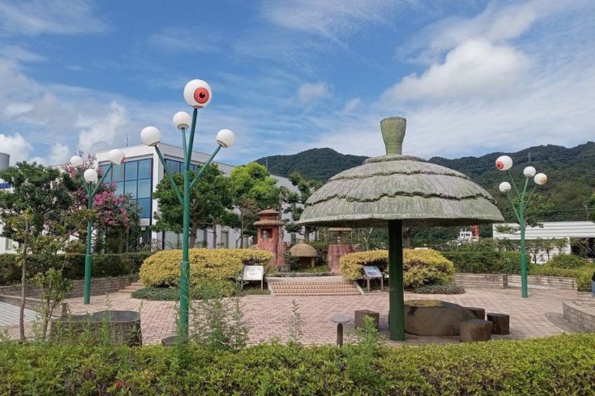 A park with a large mushroom-shaped structure, lamp posts, and a building in the background. 4
