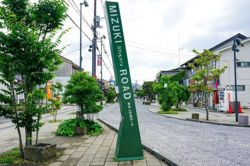 A street sign for Mizuki Shigeru Road, surrounded by trees and buildings. 3