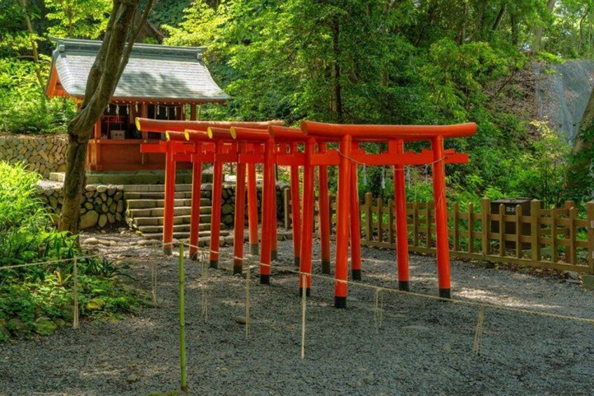 A row of red torii gates in a forested area with a traditional building in the background. 3