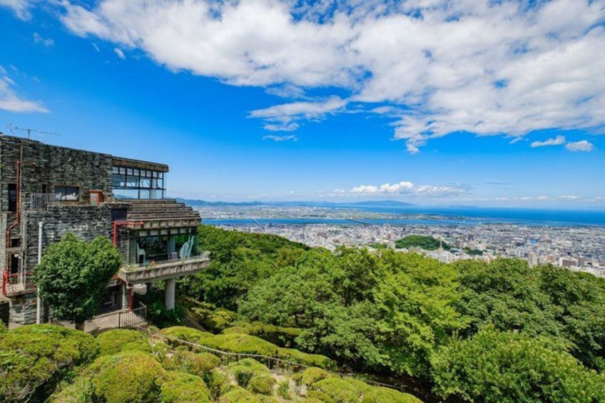 A modern building with a glass facade overlooking a city and lush greenery. 1