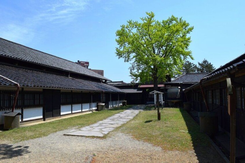 A traditional Japanese courtyard with wooden buildings, a stone pathway, and a large tree. 5