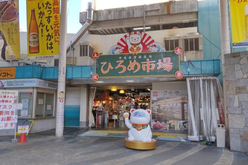 A storefront with a sign in Japanese, a large mascot statue, and a building facade with multiple windows. 3