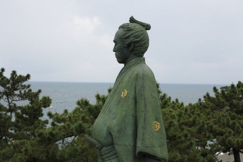 A statue of a person with a green cloak, overlooking a body of water and surrounded by trees. 4