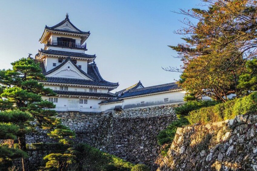 A traditional Japanese castle with multiple tiers, surrounded by lush greenery and a rocky cliff. 1
