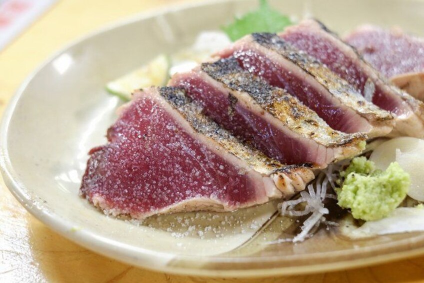 A plate of sliced tuna with a dark crust, garnished with green wasabi and shredded daikon radish. 2