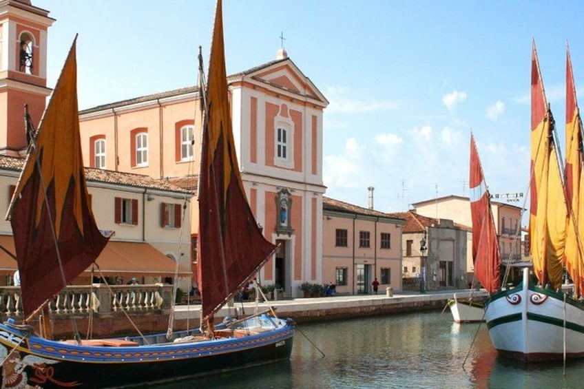 A harbor with boats, a building with a clock tower, and a clear sky. 1