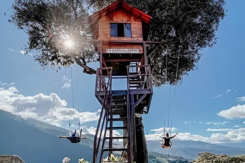 A treehouse with a red roof, a wooden staircase, and two swings. 3
