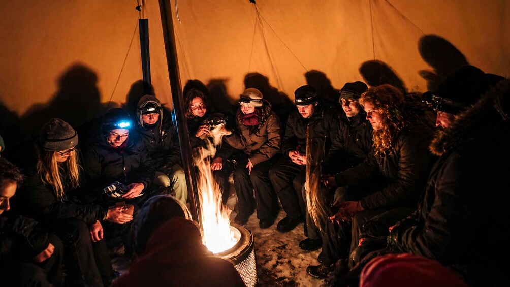 A group of people gathered around a campfire inside a tent. 3