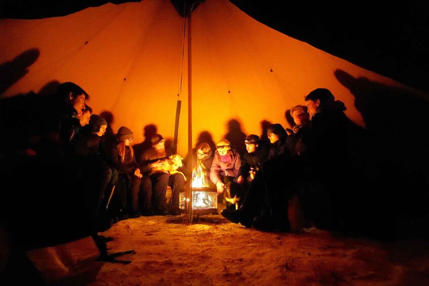 A group of people gathered around a campfire inside a tent. 5