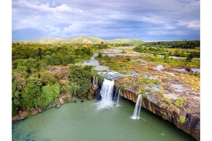 Una cascada se precipita desde un acantilado hacia un río, rodeado de abundante vegetación y colinas. 1