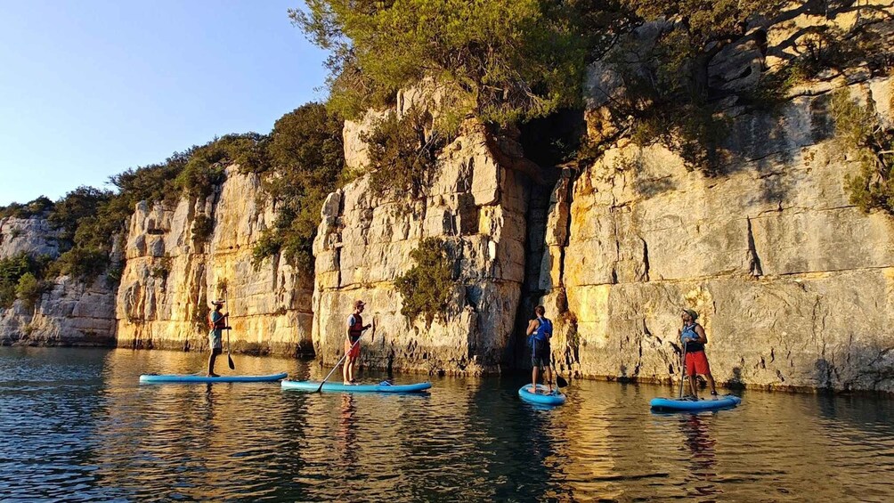 People paddleboarding near rocky cliffs with water. 2