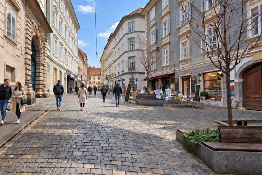 A cobblestone street lined with historic buildings, a tree, and outdoor seating. 3