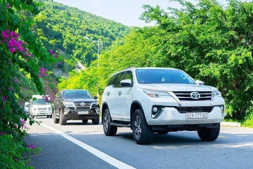 A white SUV driving on a road with a mountainous landscape in the background. 4