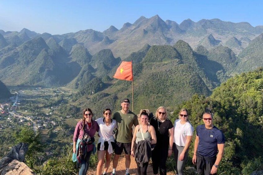 A group of people standing on a mountain with a flag, surrounded by a mountainous landscape. 3
